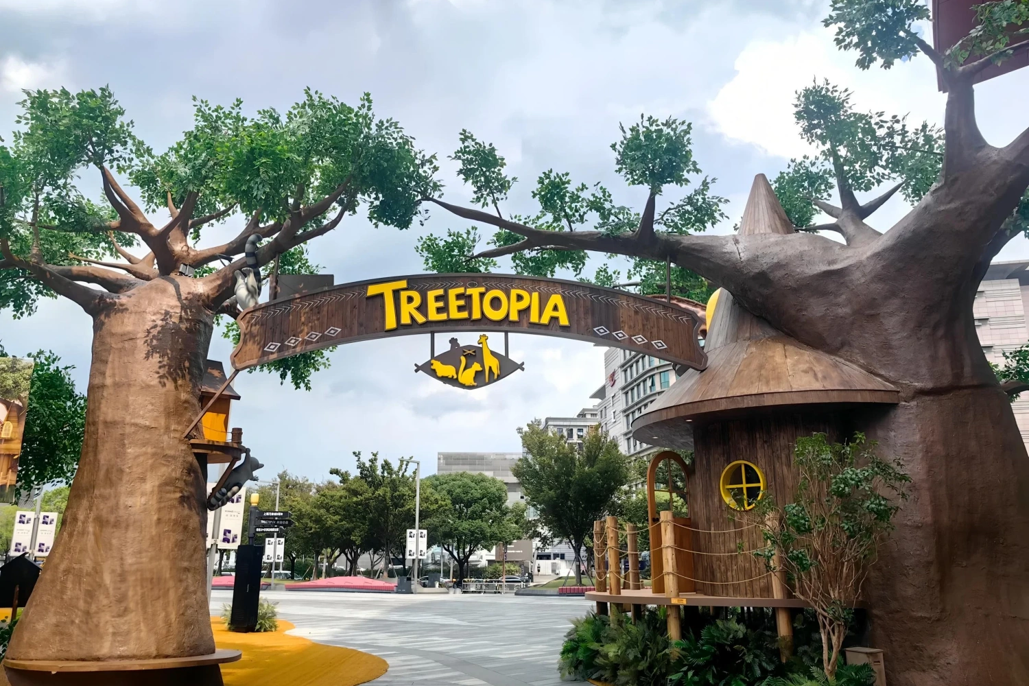 Realistic outdoor "TREETOPIA" forest theme entry archway at a commercial plaza, featuring bionic wood textures and animal silhouettes to create a natural woodland atmosphere.