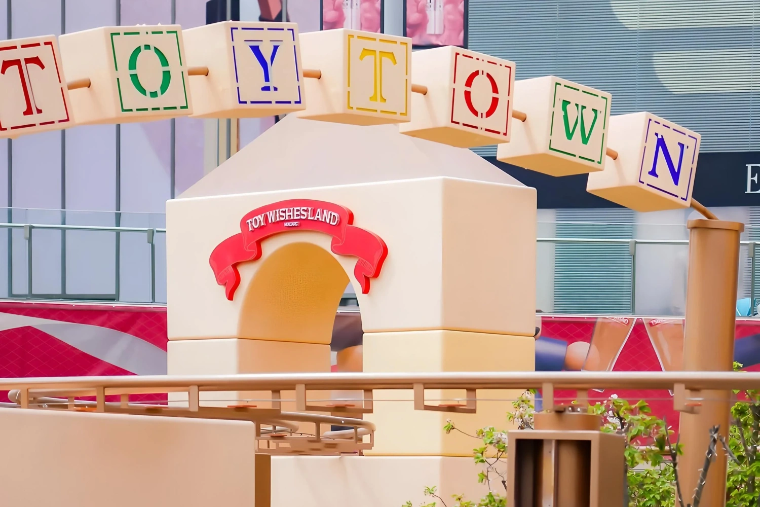 The iconic building block letter archway (TOY TOWN) of "Toy Wishesland", featuring a solid wooden frame with colorful letter blocks against a backdrop of modern commercial buildings.