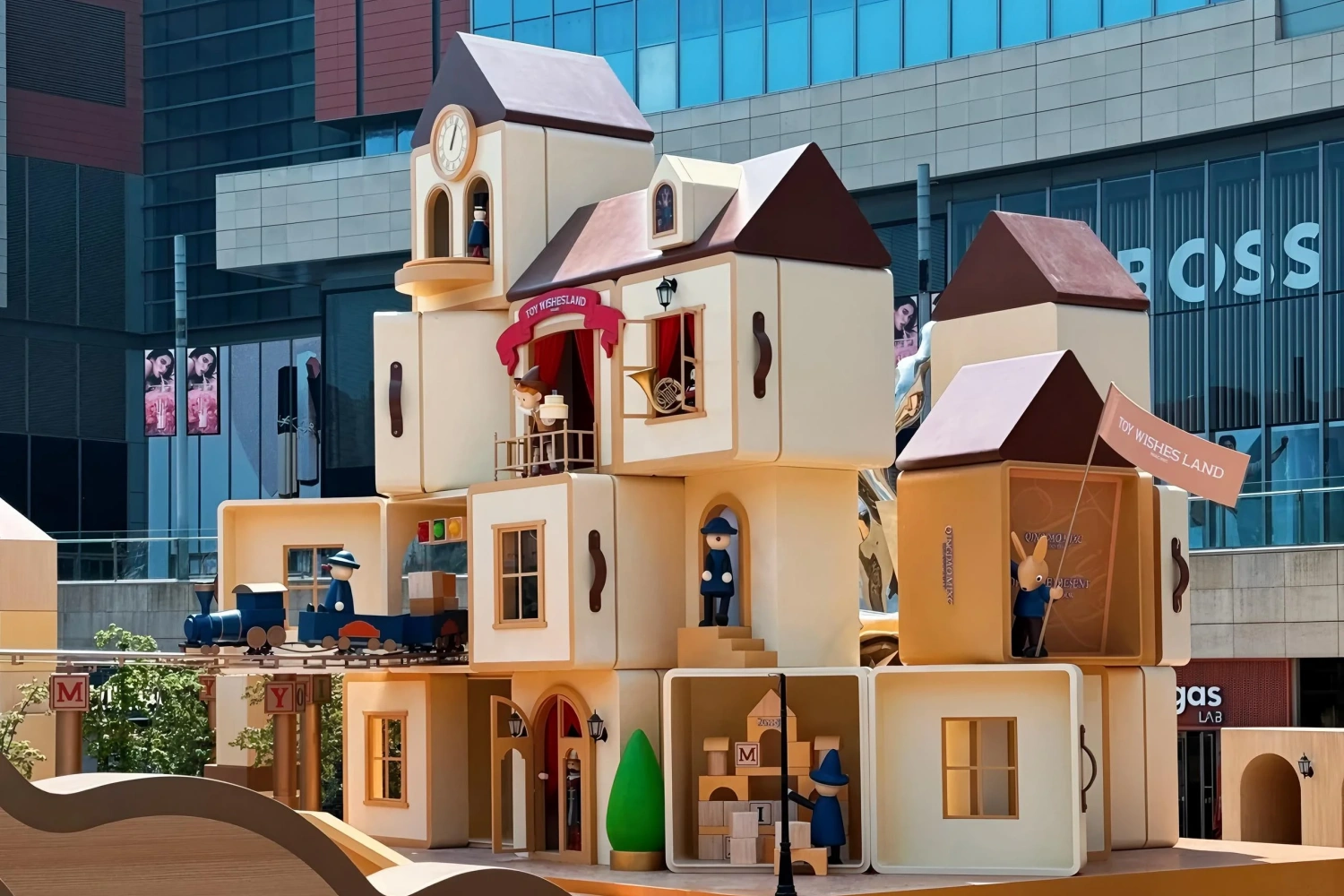 Large-scale "Toy Wishesland" visual merchandising installation in an outdoor commercial plaza, featuring details like a blue train, a bunny holding a flag, and building block signs.