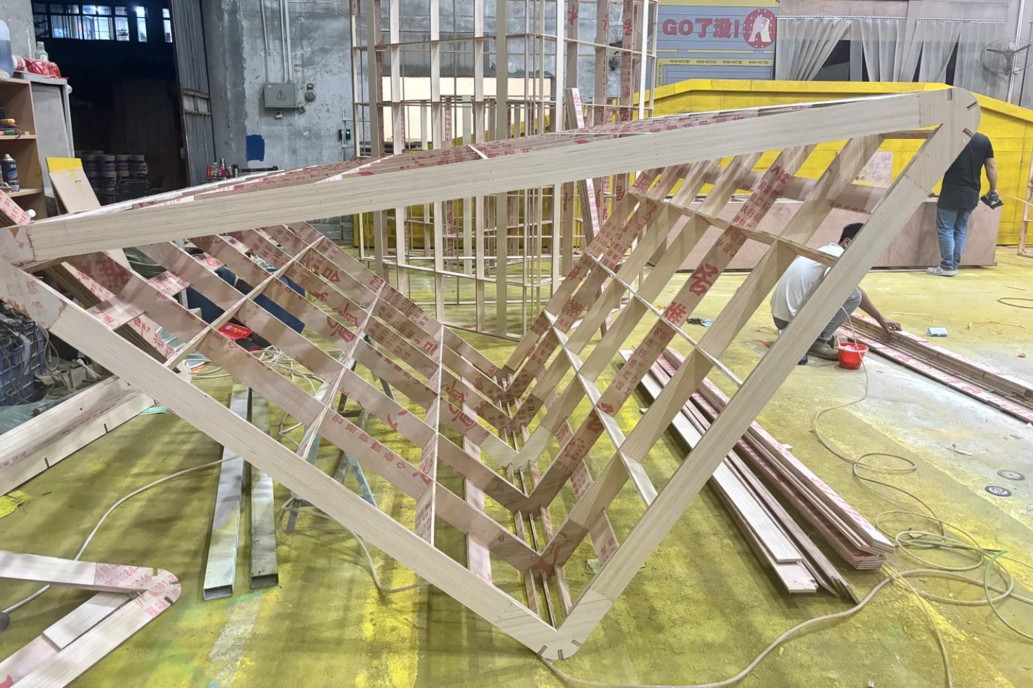 Workshop view of a mall exhibition factory, where workers are constructing the complex wooden skeleton and internal supporting frames for the toy house.