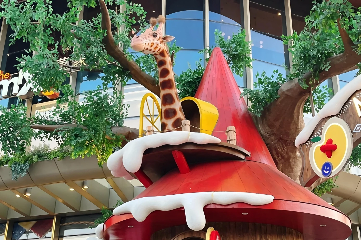 Large interactive animal landscape inside the mall, with a giraffe model leaning over the second-floor terrace above a red conical roof, accented with snow elements for a striking visual impact.