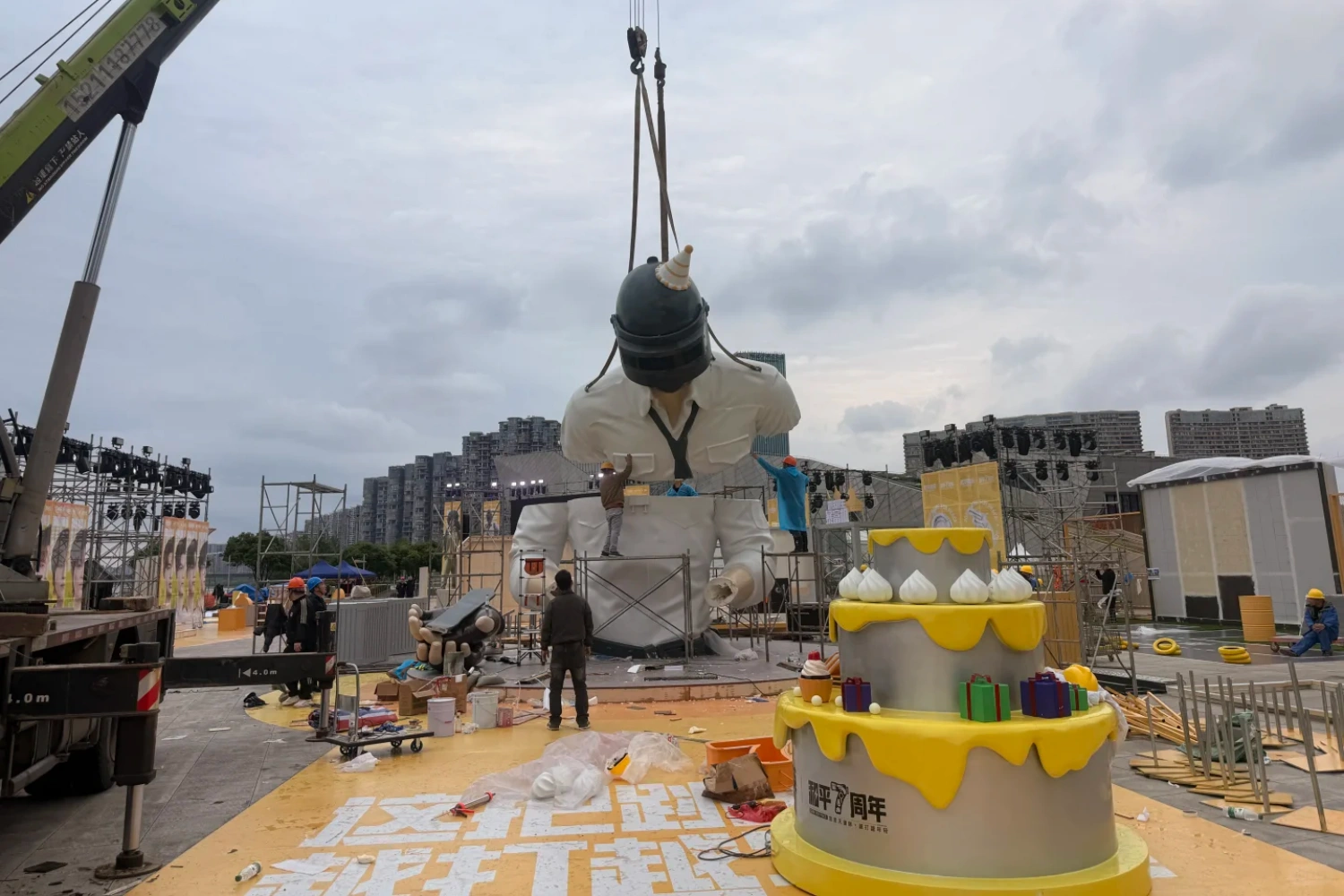 The final assembly site of the city landmark art installation. The giant IP is displayed in the center of the square, accompanied by a yellow-and-white two-tier birthday cake-shaped commercial display.