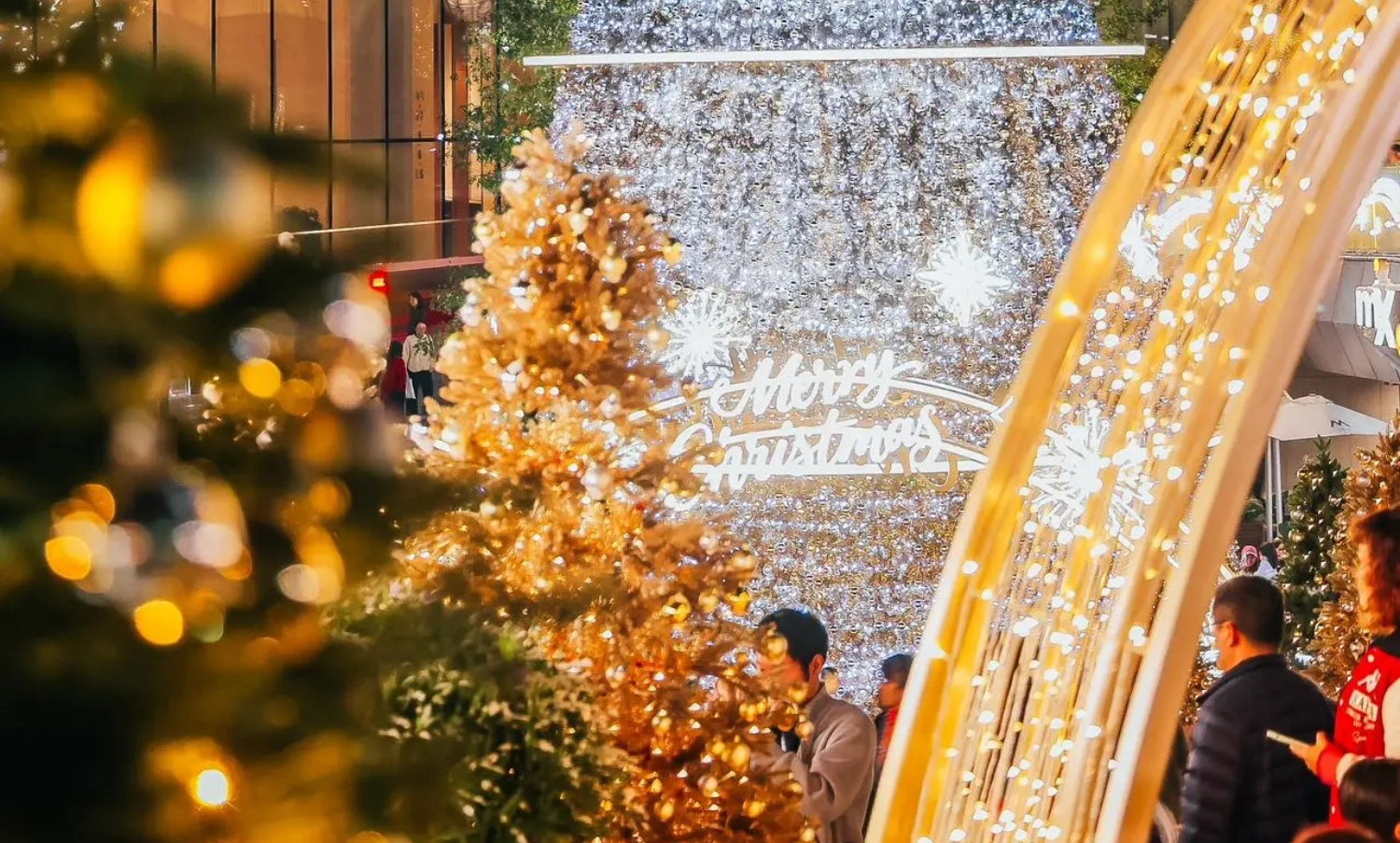 The MIXC mall's large-scale outdoor Christmas installation project, with its stunning visual volume and exquisite details, has become an influential and eye-catching winter landscape in the city. From the perspective of professional factory custom fabrication and on-site execution, this is a benchmark case integrating irregular structural processing, complex lighting engineering, and precise on-site construction solutions. Below, we provide an in-depth analysis of the project's entire execution process across five core dimensions:
1. Structural Safety: Wind Load Challenges of Ultra-High Tower Structures
The massive cone-shaped main tree stands in the center of the commercial plaza, featuring a layered ring structure design topped with a shining star decoration. As a large-scale customized outdoor commercial visual merchandising (VM) project, the primary challenge was passing the structural safety test in winter's strong wind environments. Once the main tree is heavily laden with dense ornaments and string lights, the windward resistance becomes immense, and the overall center of gravity is quite high.
During the prop fabrication phase, the factory utilized high-strength hot-dip galvanized steel for the core load-bearing skeleton, and structural engineers conducted rigorous wind load mechanics calculations. The base system employed a concealed counterweight foundation, while the upper tower body utilized modular flange bolting technology. This solid internal-to-external support ensured the absolute safety of the entire Christmas installation under extreme outdoor weather conditions.
2. Lighting & Craftsmanship Aesthetics: Seamless Arrangement of a Million-Level Starlight Matrix
The main body of the installation is covered with dense, waterfall-like cool white LED string lights, interspersed with large glowing snowflake motifs. On the other side, the "MIXC STATION" area features warm, golden-yellow lighting with a retro glow, complete with a delicate British-style double-sided clock. The outdoor lighting engineering not only requires the wiring to achieve an IP65 or higher waterproof rating, but more challenging is how to perfectly conceal the wiring among thousands of light points to maintain surface smoothness and craftsmanship aesthetics during the day when the lights are off.
The factory team customized a high-density, flame-retardant, light-transmitting mesh as the skeleton backing, and all main cables utilized an embedded, hidden wiring process. For color selection, the color temperature difference between the cool white and warm yellow lights was strictly compared. Through precise zoning, a strong visual contrast was created between the crisp snow-crystal texture and the warm, vintage atmosphere of the passageway.
3. Complete Pre-Assembly: 1:1 Precise Restoration of Irregular Components
Not only does the main tree require seamless splicing, but the smoothly curved golden archway supports and the "MIXC STATION" hanging plaque with its custom baked-enamel finish also demand extremely high dimensional accuracy. Multi-curved metal pipes are highly susceptible to stress deformation during bending and welding. Any tolerance discrepancies during on-site assembly would severely compromise the final execution of the VM design.
We comprehensively implemented a 1:1 complete pre-assembly protocol prior to factory dispatch. All curved metal structures and luminous rings underwent trial assembly in our extra-large factory workshop. The quality inspection department verified every screw hole and joint flatness one by one, proactively preventing potential alignment errors during on-site construction to ensure every module interlocked smoothly.
4. On-Site Installation & Detailing: Extreme Micro-Operations in Complex Terrain
The installation site featured a complex landscape with multi-level steps, water feature edges, and dense greenery; additionally, a giant inflatable Santa Claus was suspended from a surrounding wall. Mall installations are typically restricted to a very short time window at night after closing. Furthermore, the operating space for large hoisting equipment was limited on the multi-tiered plaza, and strict measures were required to protect the premium stone flooring from damage.
The construction team developed a highly modular, "building-block" style night operation plan. All load-bearing bases were pre-laid with custom flexible non-slip protective mats. Through the seamless coordination of heavy cranes and aerial work platforms, components were hoisted and assembled layer by layer from bottom to top according to their pre-assigned numbers. For edge detailing, custom metal skirting boards and artificial pine needles were cleverly utilized as transitional covers at the bottom edge, achieving a flawless, high-quality delivery(5)