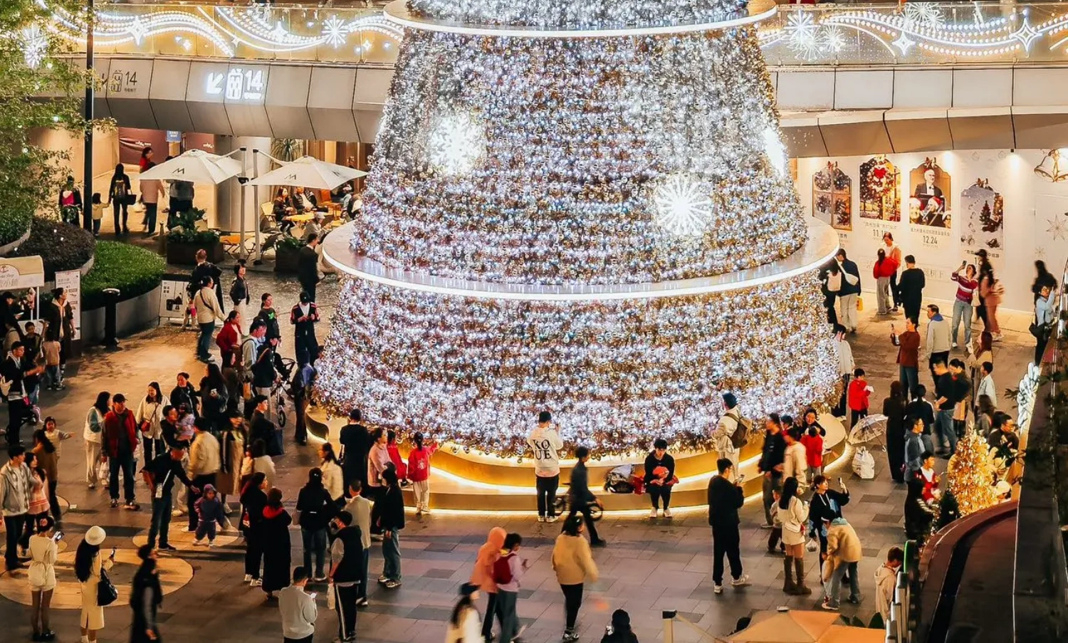 The MIXC mall's large-scale outdoor Christmas installation project, with its stunning visual volume and exquisite details, has become an influential and eye-catching winter landscape in the city. From the perspective of professional factory custom fabrication and on-site execution, this is a benchmark case integrating irregular structural processing, complex lighting engineering, and precise on-site construction solutions. Below, we provide an in-depth analysis of the project's entire execution process across five core dimensions:
1. Structural Safety: Wind Load Challenges of Ultra-High Tower Structures
The massive cone-shaped main tree stands in the center of the commercial plaza, featuring a layered ring structure design topped with a shining star decoration. As a large-scale customized outdoor commercial visual merchandising (VM) project, the primary challenge was passing the structural safety test in winter's strong wind environments. Once the main tree is heavily laden with dense ornaments and string lights, the windward resistance becomes immense, and the overall center of gravity is quite high.
During the prop fabrication phase, the factory utilized high-strength hot-dip galvanized steel for the core load-bearing skeleton, and structural engineers conducted rigorous wind load mechanics calculations. The base system employed a concealed counterweight foundation, while the upper tower body utilized modular flange bolting technology. This solid internal-to-external support ensured the absolute safety of the entire Christmas installation under extreme outdoor weather conditions.
2. Lighting & Craftsmanship Aesthetics: Seamless Arrangement of a Million-Level Starlight Matrix
The main body of the installation is covered with dense, waterfall-like cool white LED string lights, interspersed with large glowing snowflake motifs. On the other side, the "MIXC STATION" area features warm, golden-yellow lighting with a retro glow, complete with a delicate British-style double-sided clock. The outdoor lighting engineering not only requires the wiring to achieve an IP65 or higher waterproof rating, but more challenging is how to perfectly conceal the wiring among thousands of light points to maintain surface smoothness and craftsmanship aesthetics during the day when the lights are off.
The factory team customized a high-density, flame-retardant, light-transmitting mesh as the skeleton backing, and all main cables utilized an embedded, hidden wiring process. For color selection, the color temperature difference between the cool white and warm yellow lights was strictly compared. Through precise zoning, a strong visual contrast was created between the crisp snow-crystal texture and the warm, vintage atmosphere of the passageway.
3. Complete Pre-Assembly: 1:1 Precise Restoration of Irregular Components
Not only does the main tree require seamless splicing, but the smoothly curved golden archway supports and the "MIXC STATION" hanging plaque with its custom baked-enamel finish also demand extremely high dimensional accuracy. Multi-curved metal pipes are highly susceptible to stress deformation during bending and welding. Any tolerance discrepancies during on-site assembly would severely compromise the final execution of the VM design.
We comprehensively implemented a 1:1 complete pre-assembly protocol prior to factory dispatch. All curved metal structures and luminous rings underwent trial assembly in our extra-large factory workshop. The quality inspection department verified every screw hole and joint flatness one by one, proactively preventing potential alignment errors during on-site construction to ensure every module interlocked smoothly.
4. On-Site Installation & Detailing: Extreme Micro-Operations in Complex Terrain
The installation site featured a complex landscape with multi-level steps, water feature edges, and dense greenery; additionally, a giant inflatable Santa Claus was suspended from a surrounding wall. Mall installations are typically restricted to a very short time window at night after closing. Furthermore, the operating space for large hoisting equipment was limited on the multi-tiered plaza, and strict measures were required to protect the premium stone flooring from damage.
The construction team developed a highly modular, "building-block" style night operation plan. All load-bearing bases were pre-laid with custom flexible non-slip protective mats. Through the seamless coordination of heavy cranes and aerial work platforms, components were hoisted and assembled layer by layer from bottom to top according to their pre-assigned numbers. For edge detailing, custom metal skirting boards and artificial pine needles were cleverly utilized as transitional covers at the bottom edge, achieving a flawless, high-quality delivery(6)